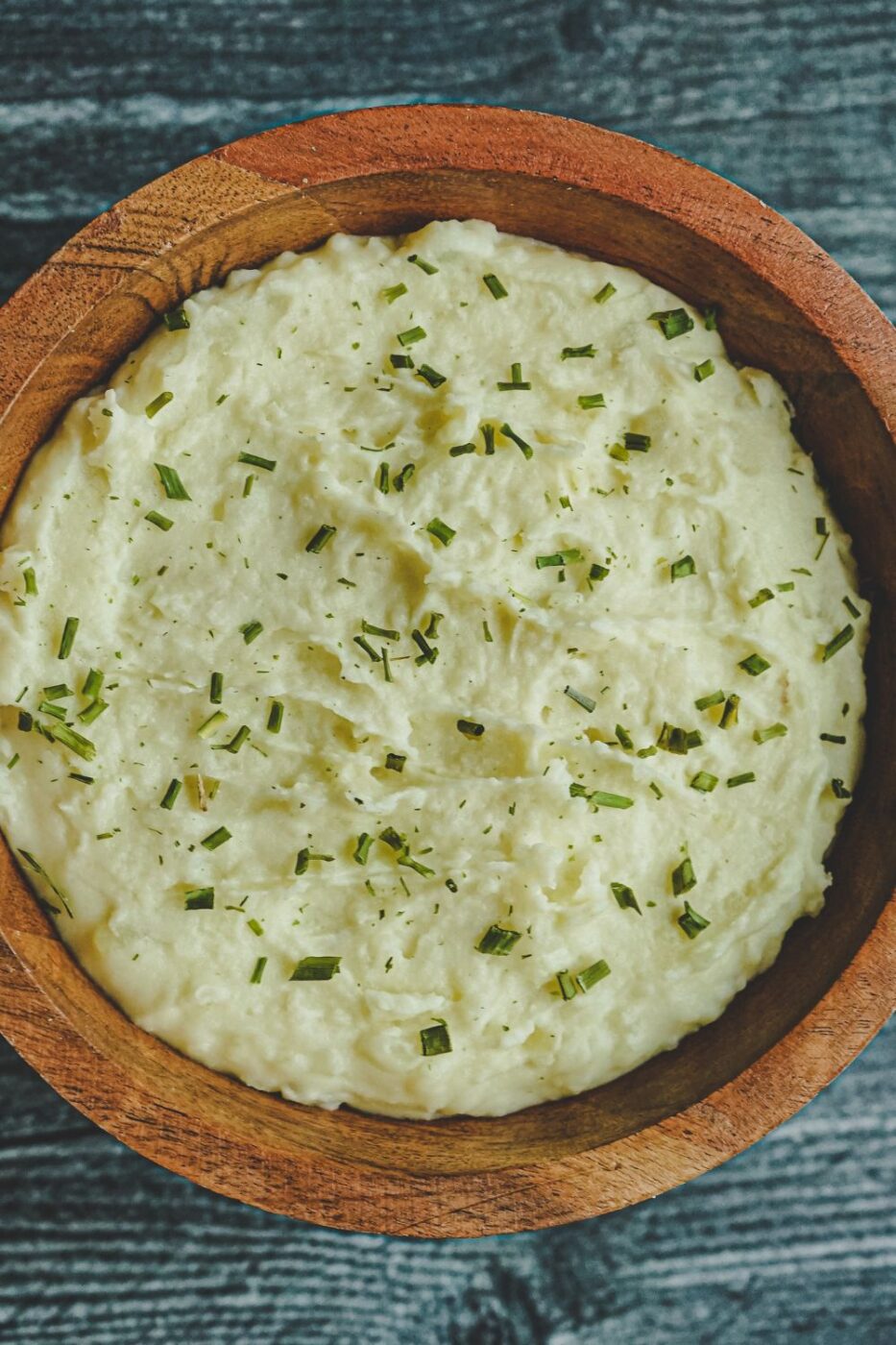 A bowl of creamy, buttery mashed potatoes with sour cream, garnished with fresh herbs for a classic comfort food dish.