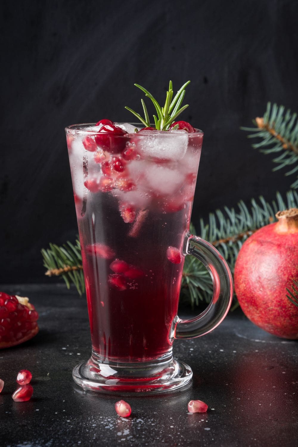 A glass of cranberry prosecco cocktail garnished with fresh cranberries and a sprig of rosemary, on a black table.