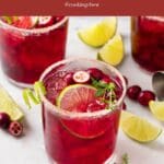 A close-up of cranberry cocktail in a glass garnished with lime and cranberry.