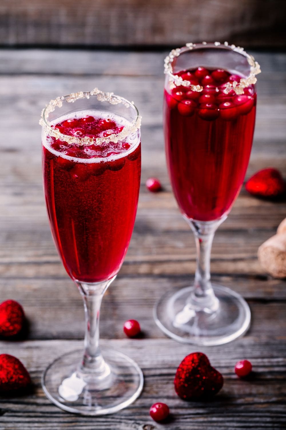 Two glasses of cranberry prosecco cocktail on a wooden table, garnished with fresh cranberries.