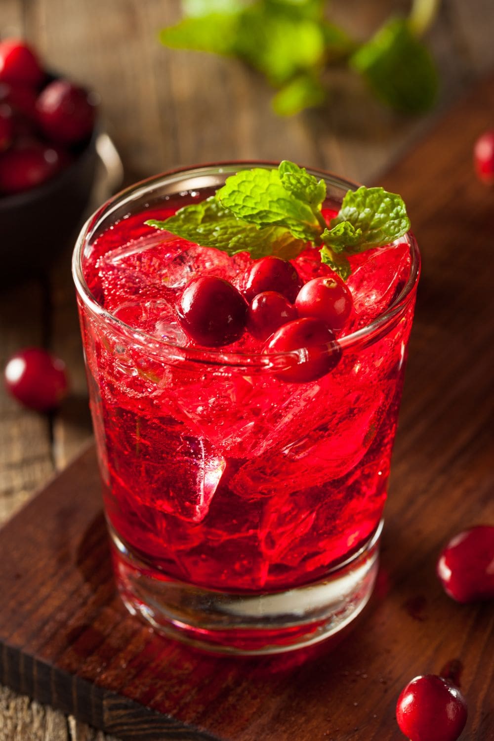 A glass of vodka cranberry cocktail garnished cranberry and mint.