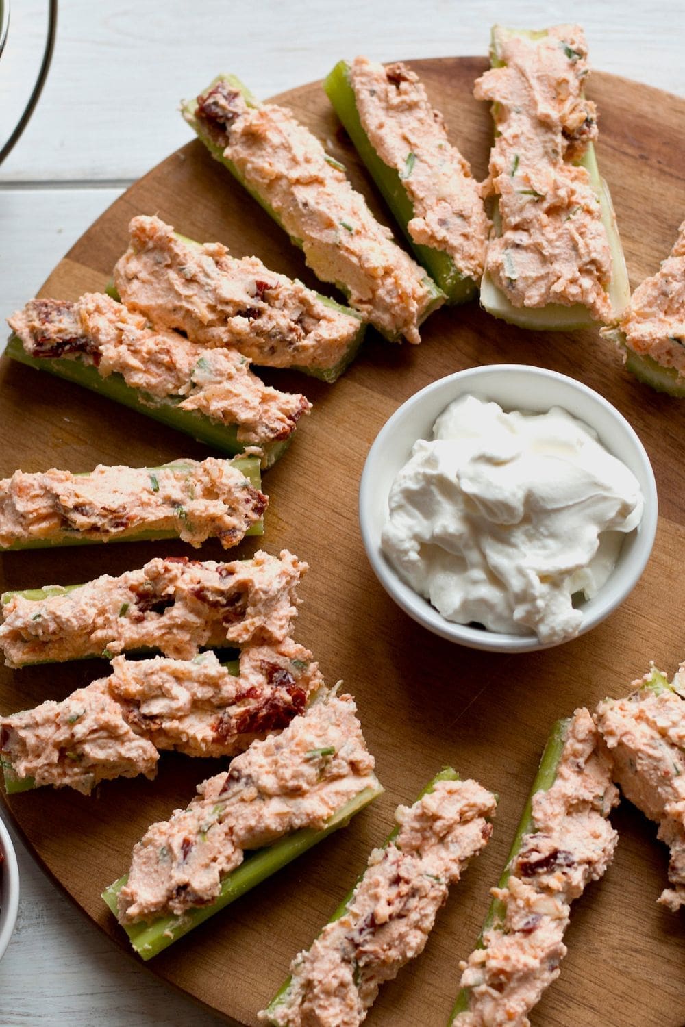 A wooden platter topped with celery sticks filled with crab meat mixture and a bowl of sour cream.