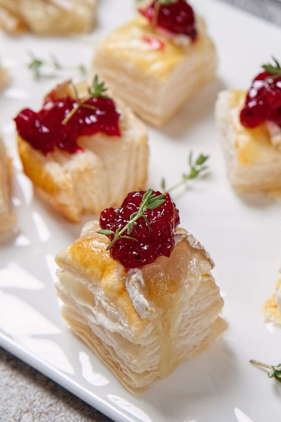 A plate of cranberry brie bites, made with puff pastry filled with cranberry sauce and brie cheese, baked until golden brown, and served warm.