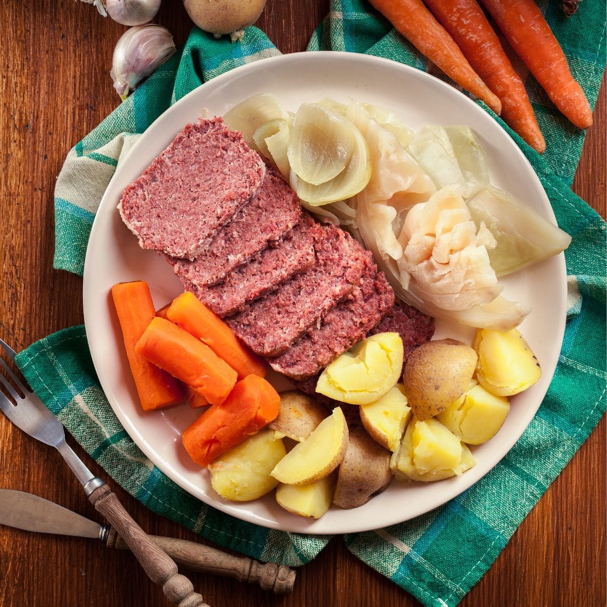 A plate of corned beef, carrots, potatoes, and cabbage on a wooden table.