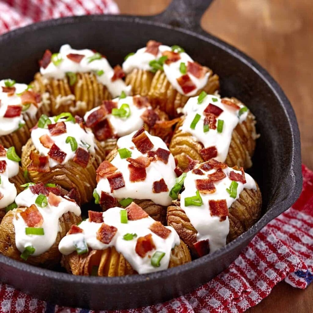 Hassleback potatoes topped with sour cream, bacon and chives served in a cast iron skillet.