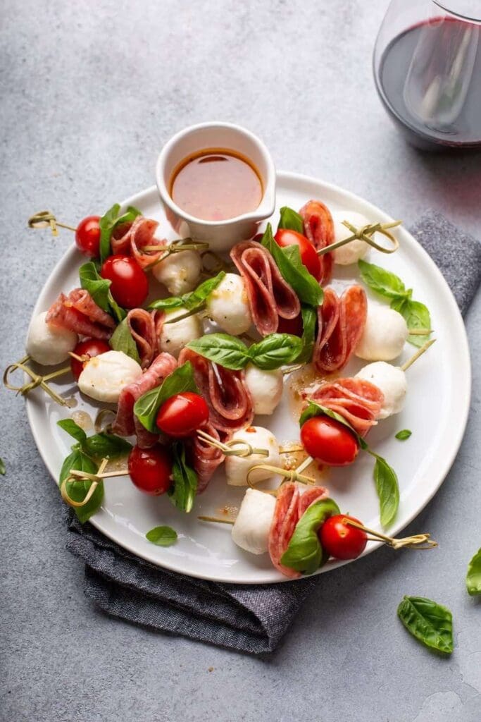 Antipasto skewers on a white plater. They made of mozzarella cheese balls, basil and tomatoes.