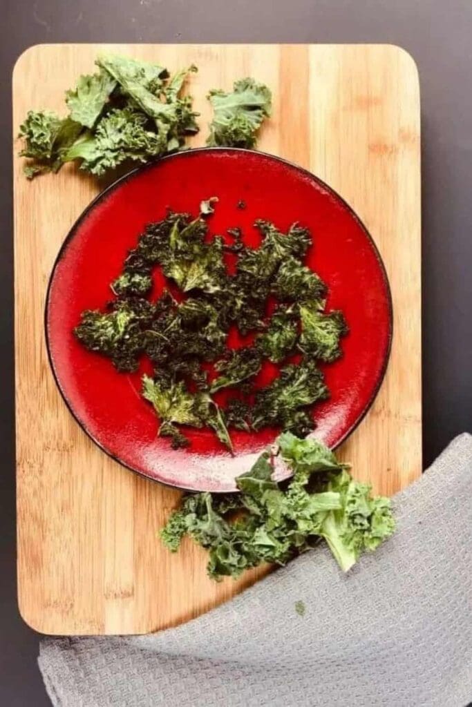 Homemade kale chips on a red plate. It is all sitting on a wood cutting board