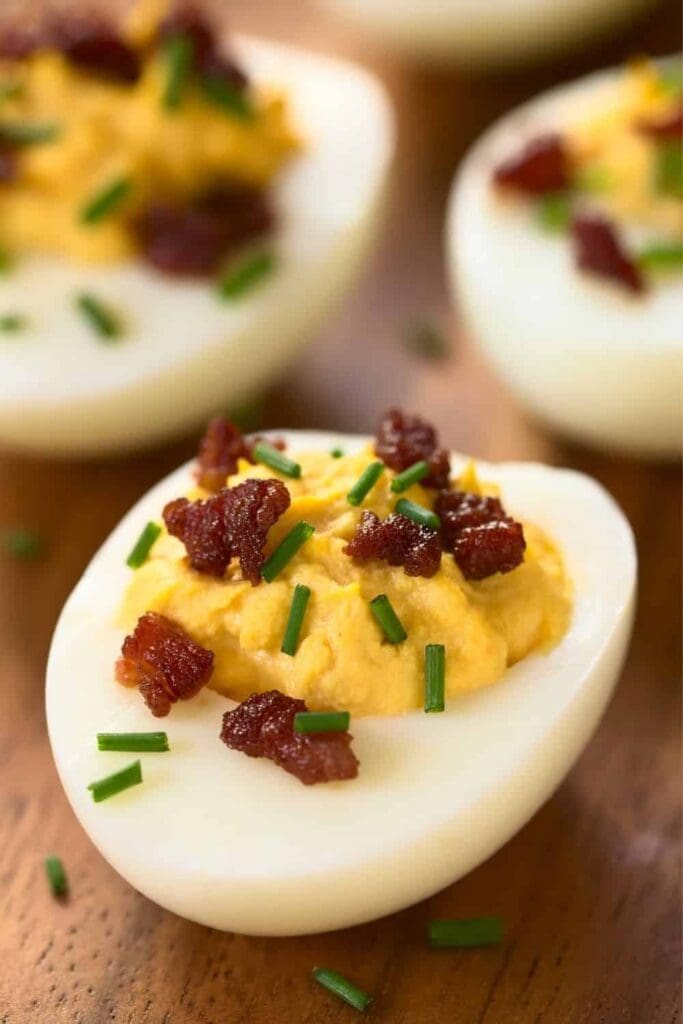 Deviled eggs with bacon and chives on top of them.