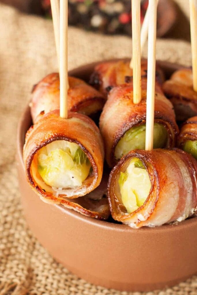 Bacon wrapped brussel sprouts in a wooden bowl. The appetizer is poked with toothpicks