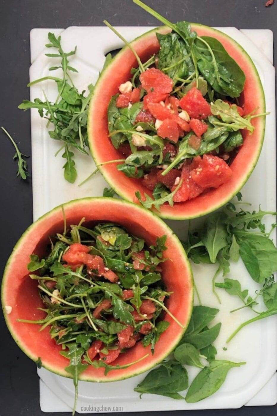 A bowl of watermelon, feta, and arugula salad with a balsamic reduction drizzle. The salad is garnished with fresh mint leaves.