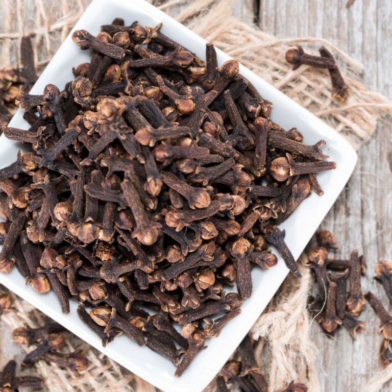 A close-up photo of a bowl of dried cloves on a wooden table
