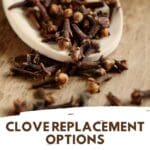 A wooden spoon overflowing with dried clove buds on a light wooden table.