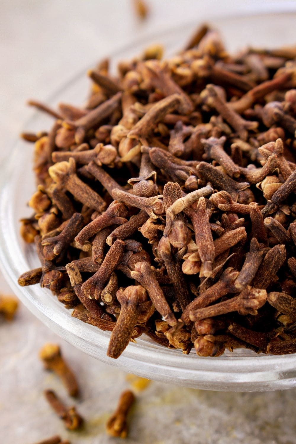 A close-up photo of a glass bowl filled with whole cloves on a wooden table.