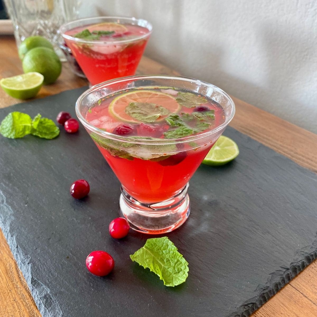 A close-up photo of a cranberry mojito in a cocktail glass garnished with a lime wedge, cranberries, and mint leaves.
