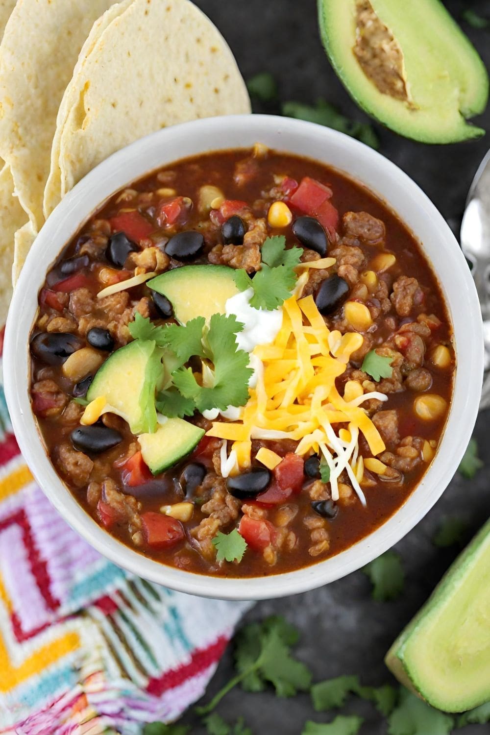 A photo of a bowl of instant pot taco soup with avocado slices, cheese, and cilantro on top.