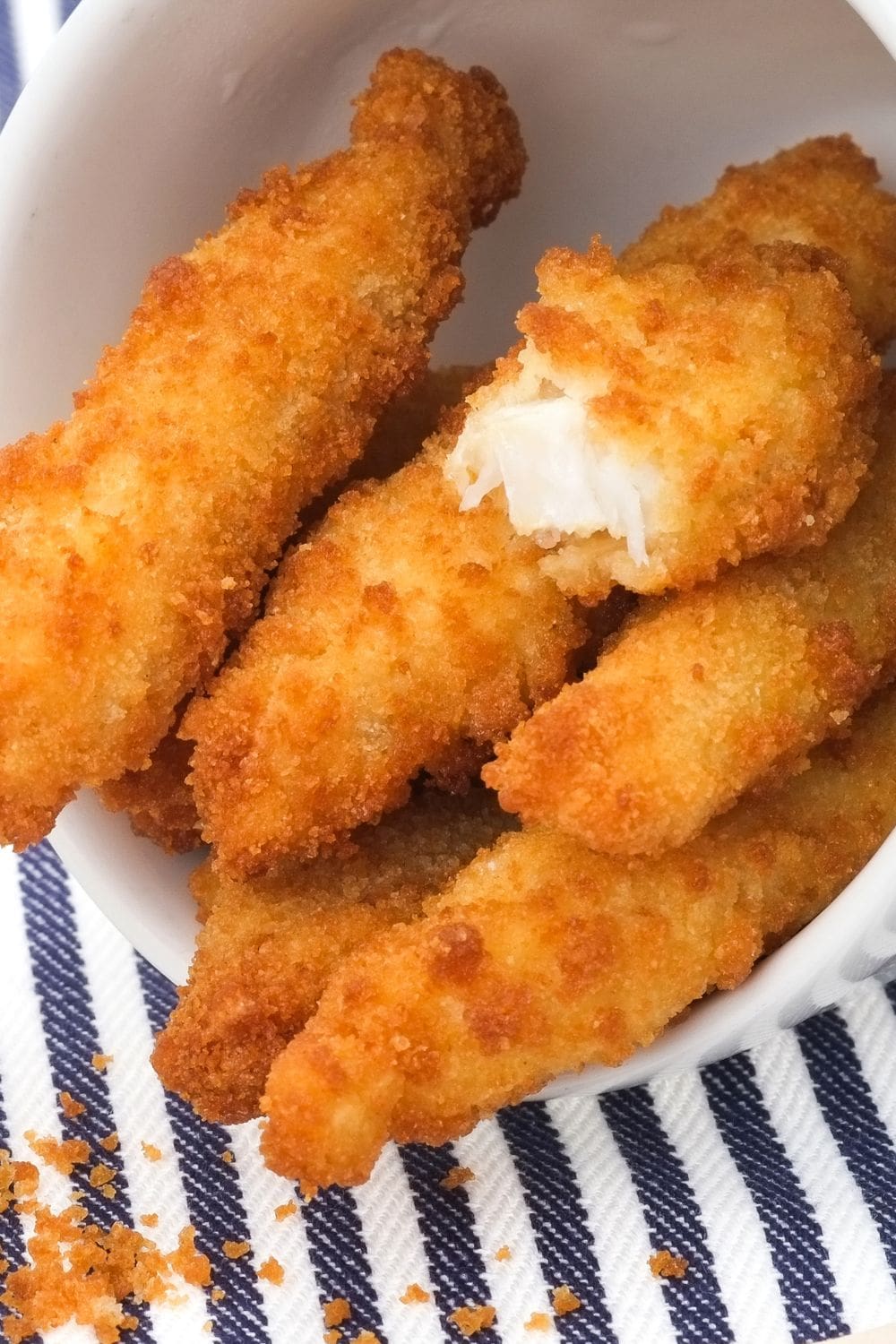A white bowl filled with golden air-fried fish sticks, resting on a blue and white striped napkin.