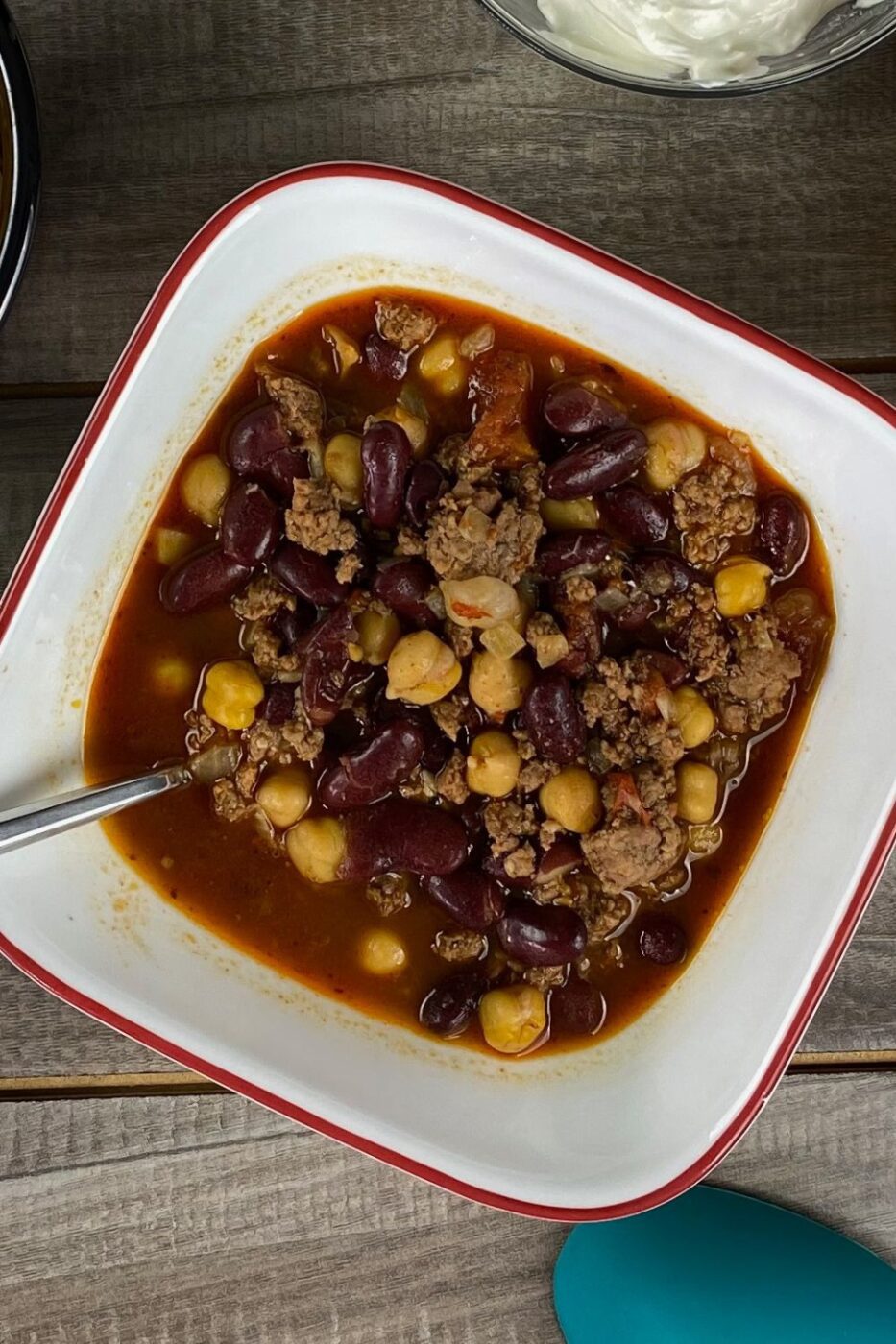 A bowl of hearty 3 bean chili topped with sour cream and herbs, served with cornbread on the side.