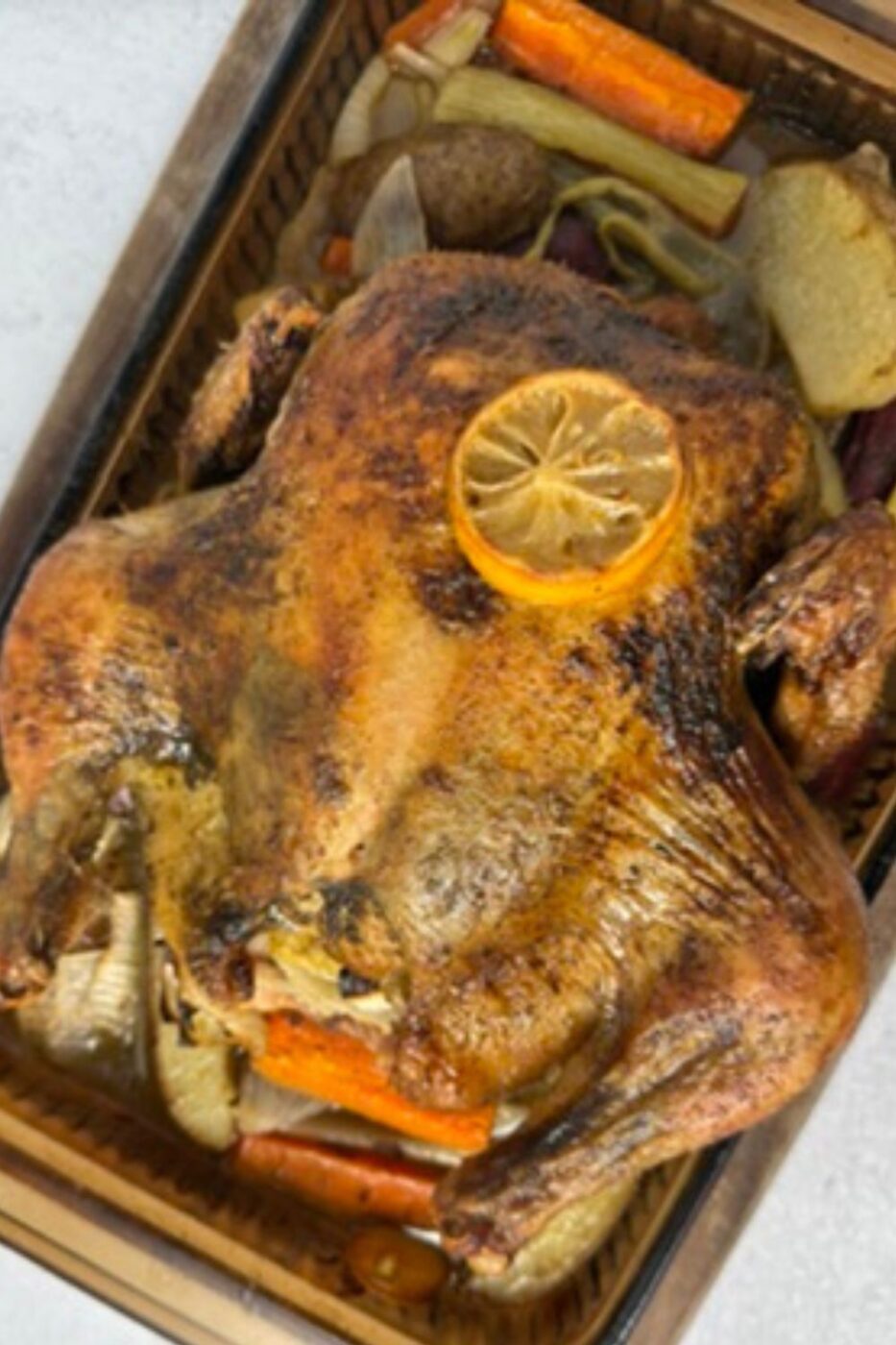 Golden-brown whole roasted chicken in a cast iron skillet, garnished with herbs and lemon slices.