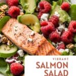 A plate of grilled salmon salad with raspberries, avocado, and spinach on a white plate.