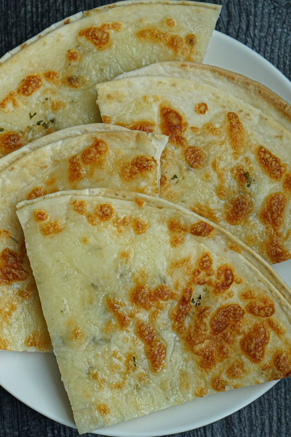 Crispy golden brown tortilla garlic bread slices topped with melted cheese and herbs, fresh from an air fryer.