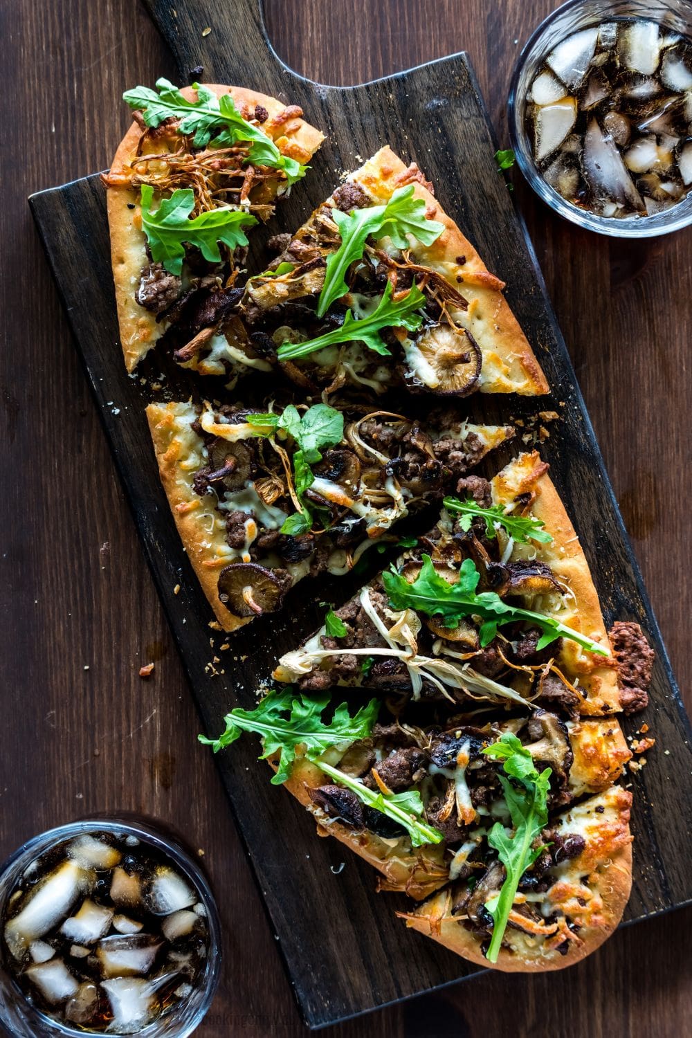 A sliced mushroom and beef flatbread pizza with arugula.