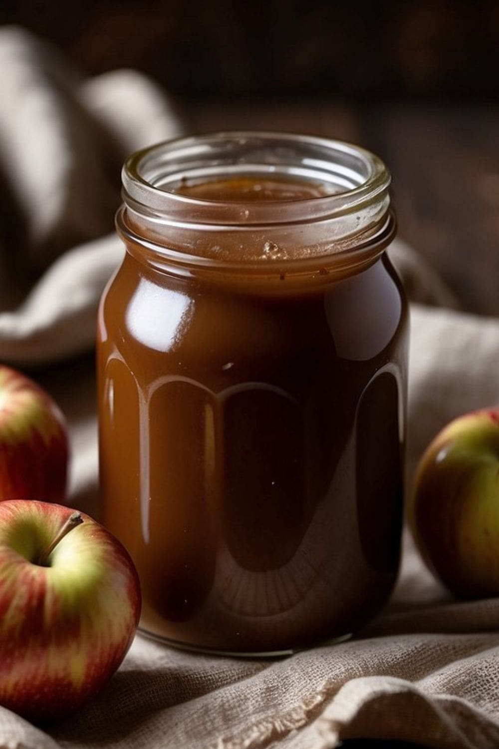 A photo of a glass jar of apple butter and red apples.