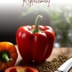 A red bell pepper, cut in half and lying on its side, rests on a wooden cutting board.