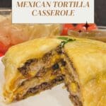 A homemade Mexican tortilla casserole dish on a plate, with a triangular slice missing from one corner.