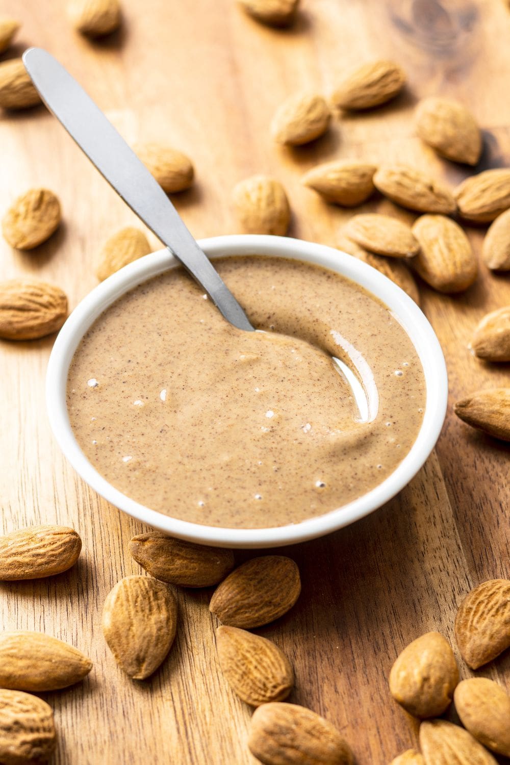 A wooden bowl of almond butter surrounded by whole almonds on a wooden table.