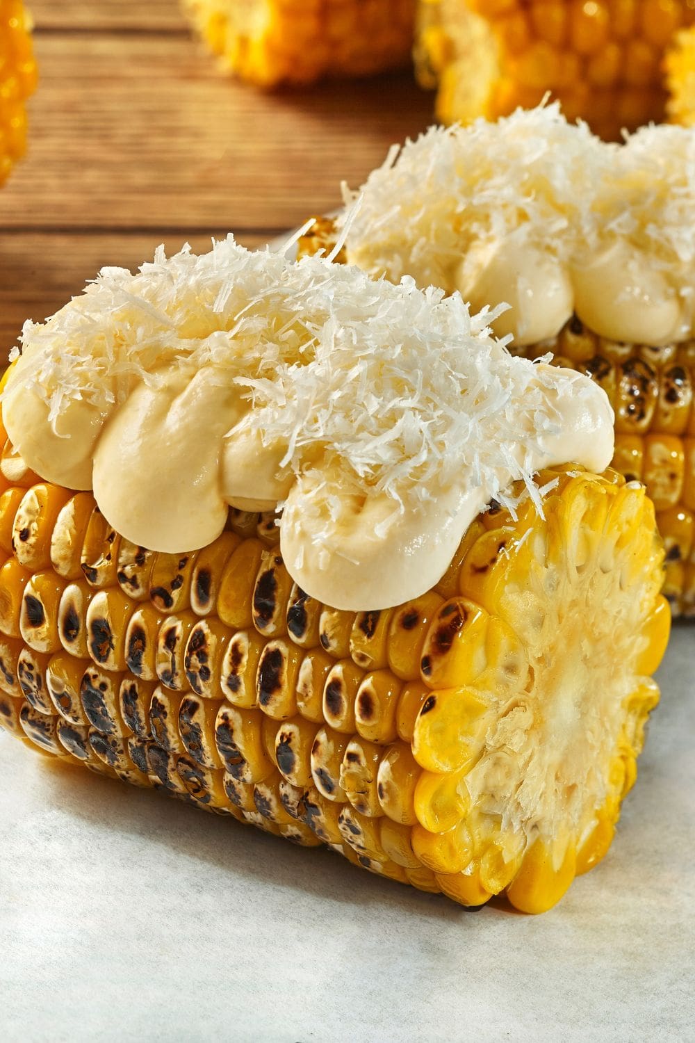A close-up photo of a grilled corn cob topped with white grated cotija cheese and a dollop of white sauce.