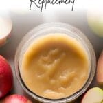 A jar of applesauce surrounded by apples.