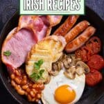 A skillet filled with a full Irish breakfast, including sausages, fried eggs, baked beans, grilled tomato slices, and slices of brown bread.