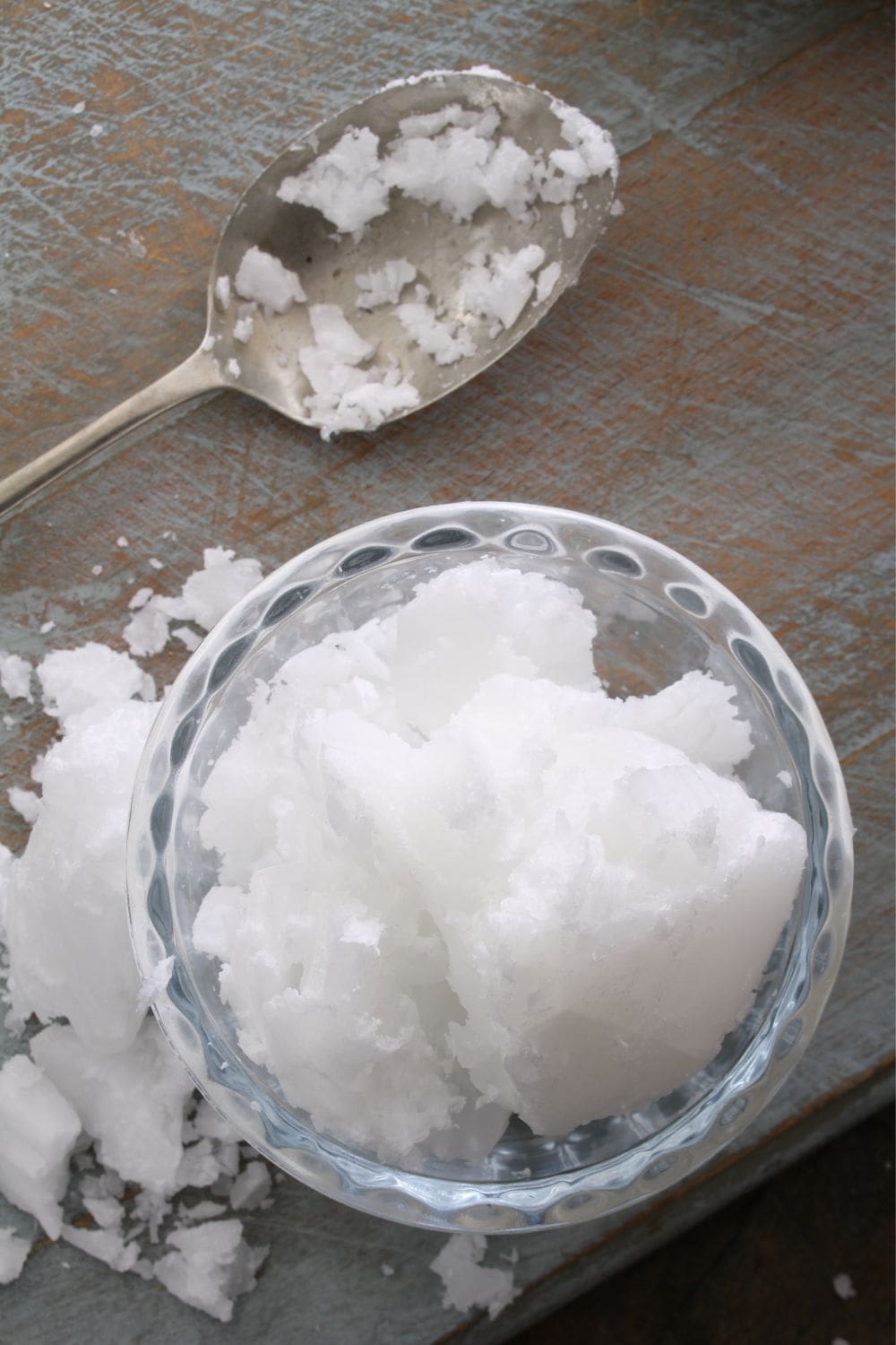 A photo of a glass bowl of coconut oil and a spoon on a wooden table.
