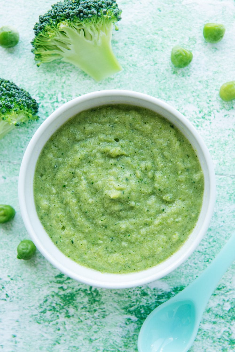 A close-up photo of a bowl of pureed broccoli and peas baby food.