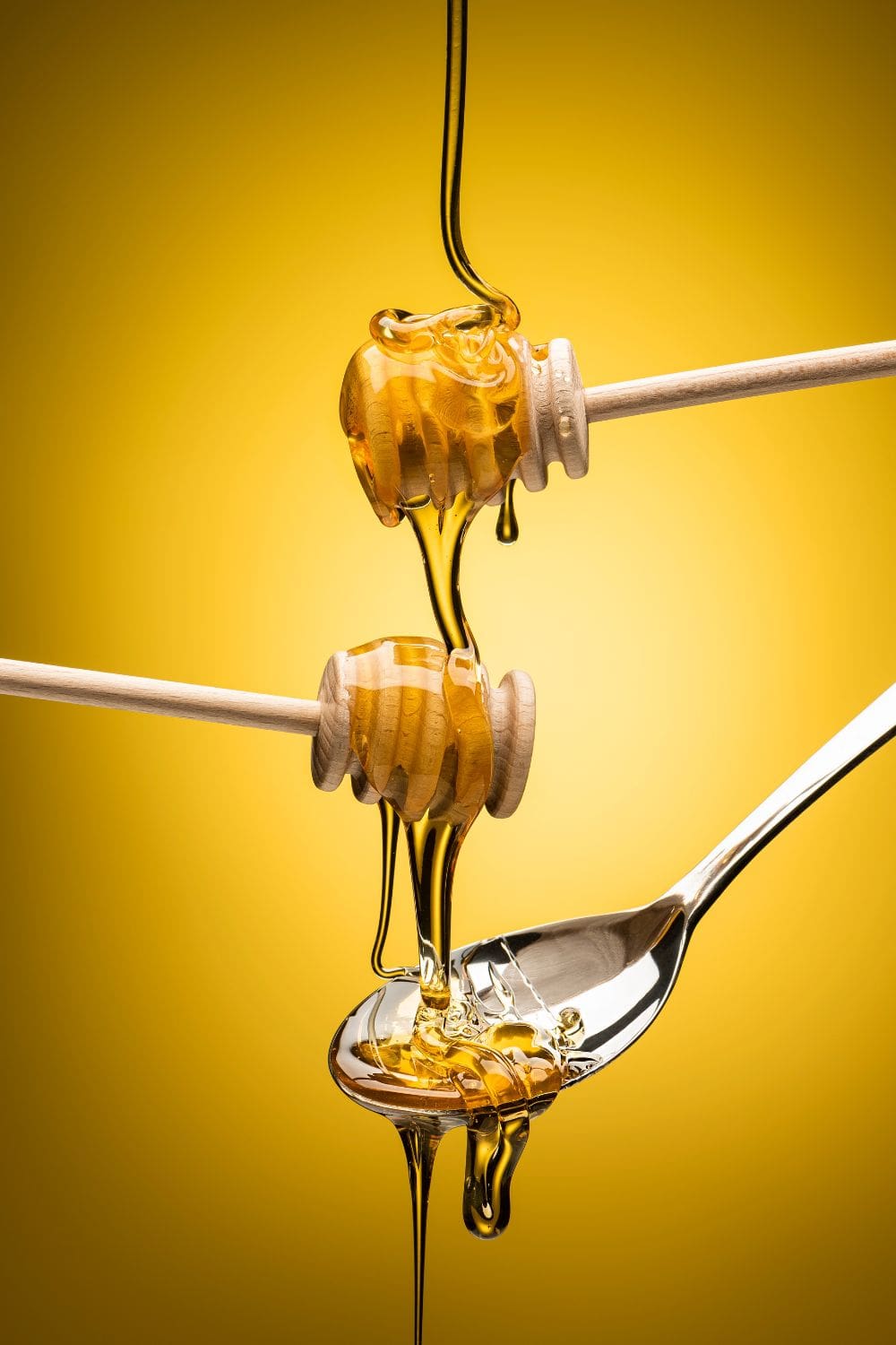 A close-up photo of a spoon filled with honey dripping from a wooden honey dipper. 