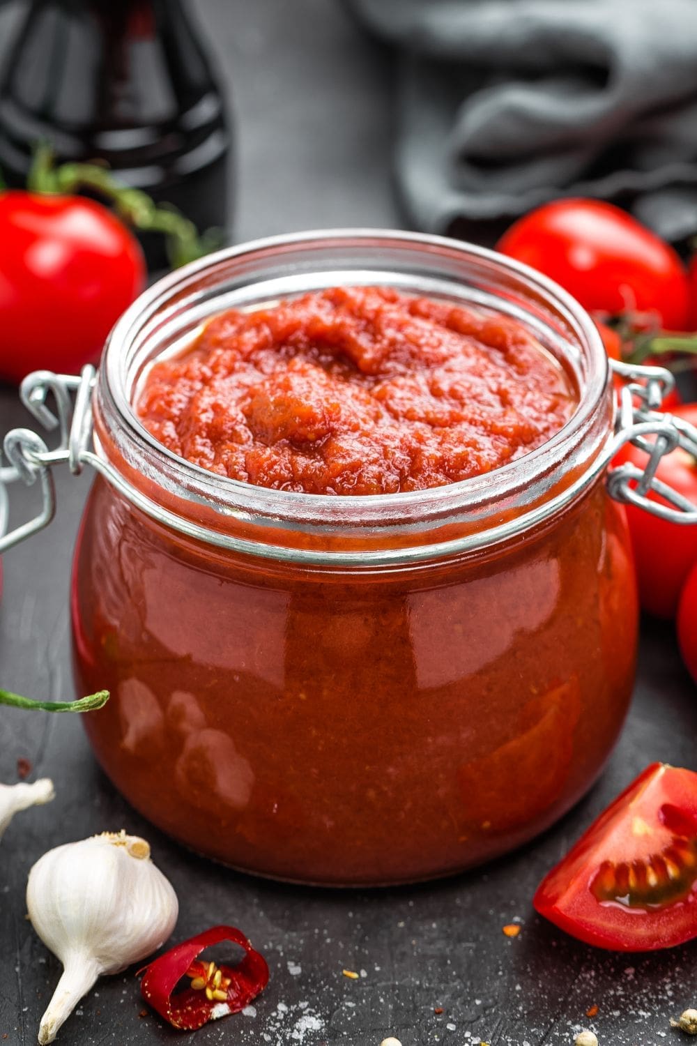 A close-up photo of a jar of tomato sauce next to tomatoes and garlic on a table.