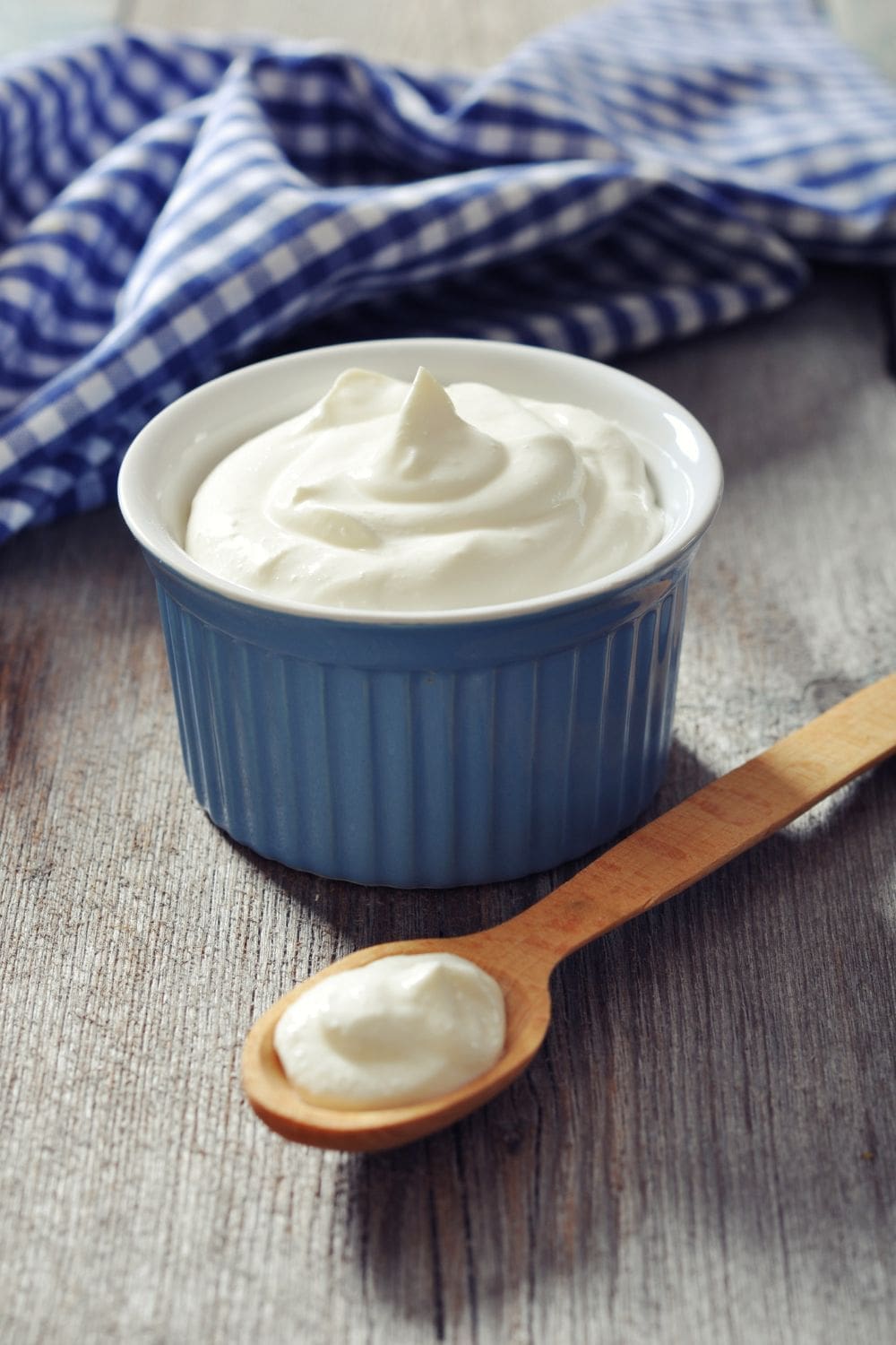 A bowl of yogurt next to a wooden spoon.