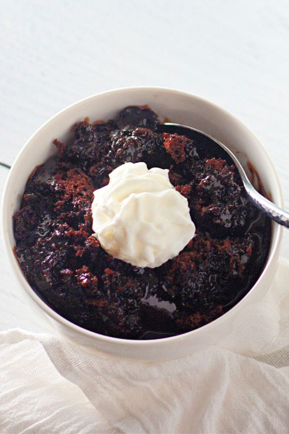 A small ramekin or mug with a warm, gooey chocolate lava cake, with a spoon digging into the center.