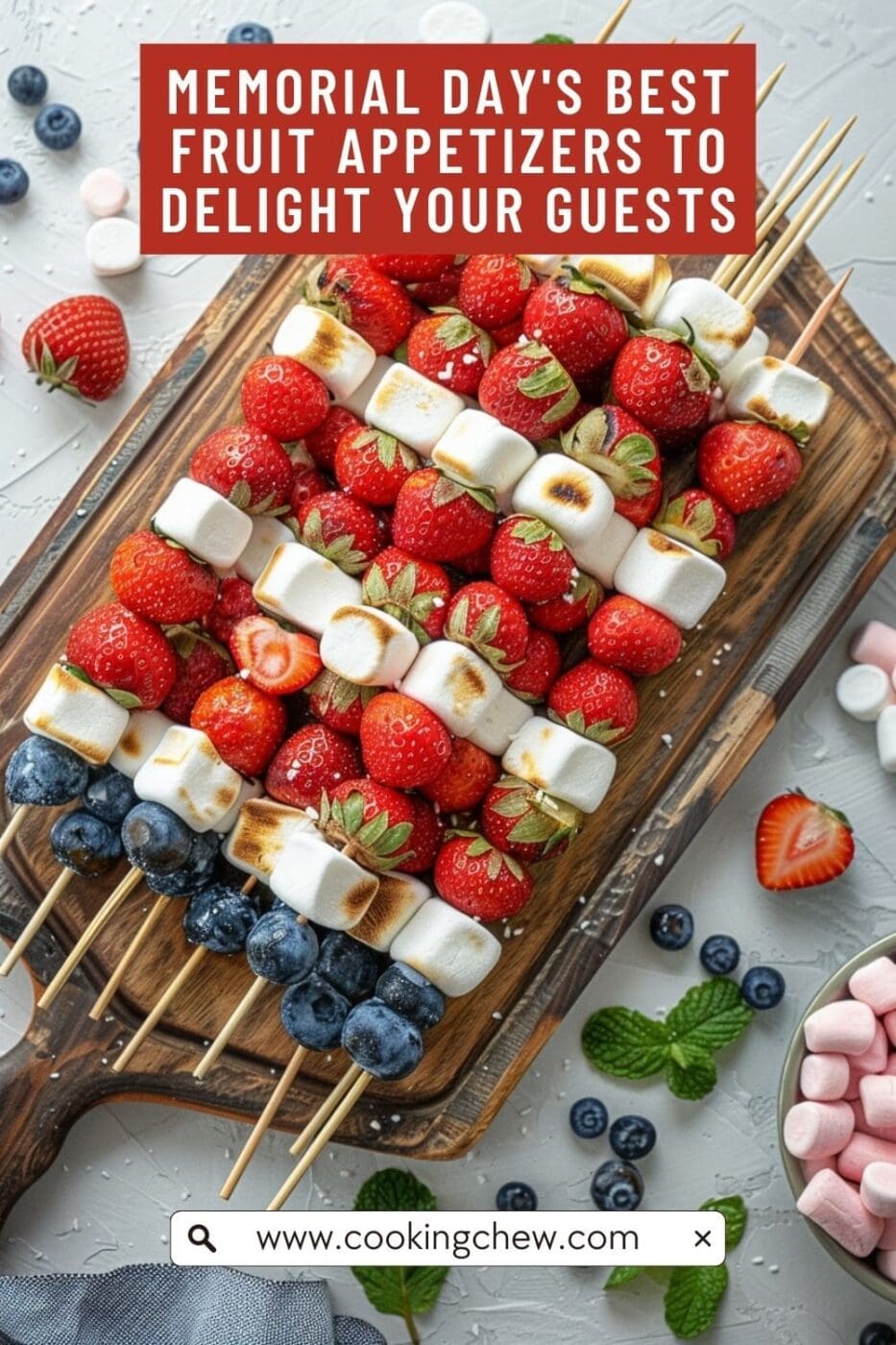 A wooden cutting board with skewers arranged in the colors of the American flag. The skewers are made with blueberries, strawberries, and marshmallows.
