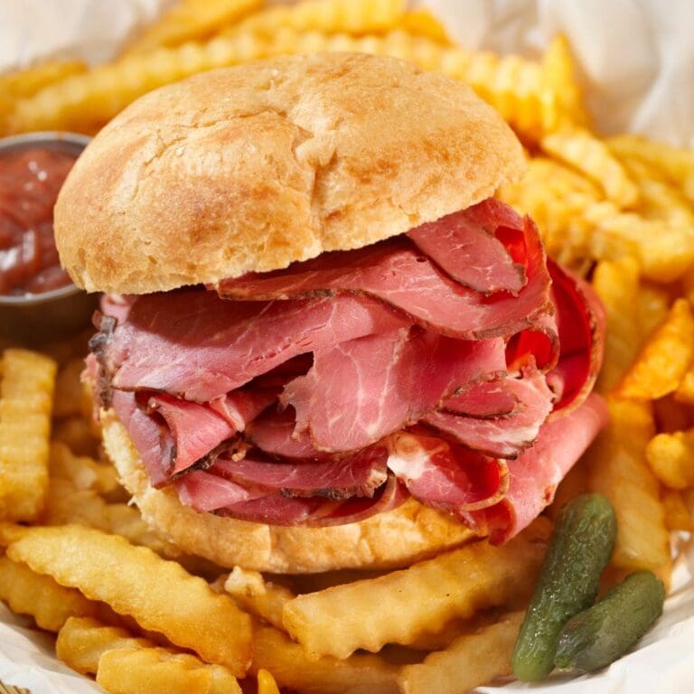 A plate with a corned beef sandwich on top of a pile of french fries.