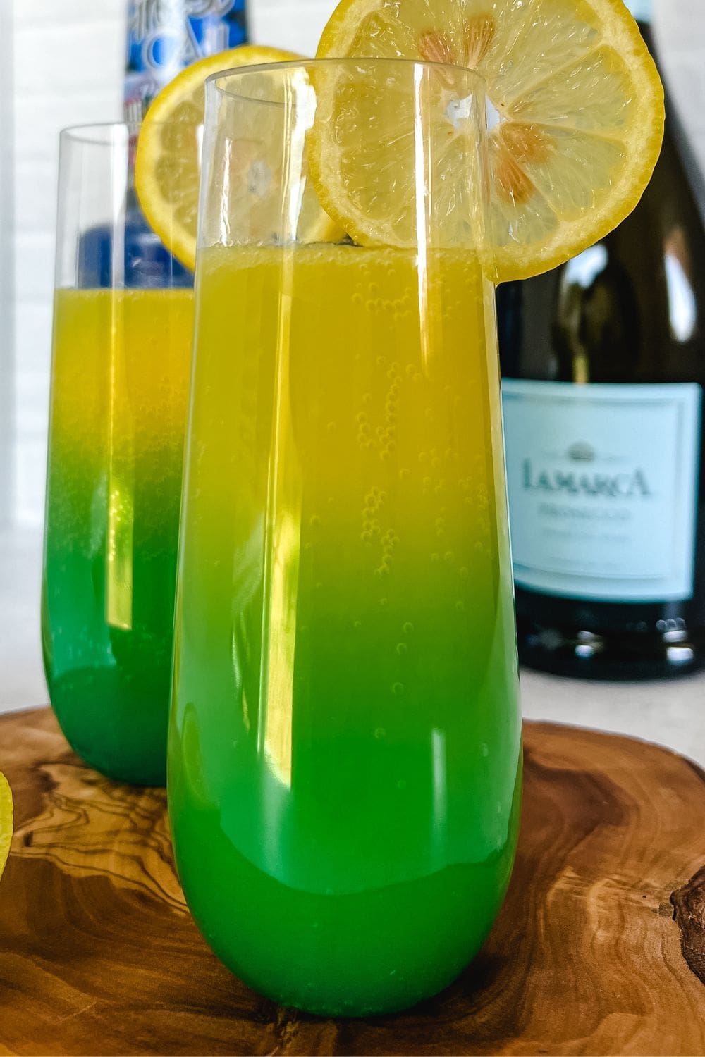 Two glasses of green mimosa with lemon slices on a wooden tray. 