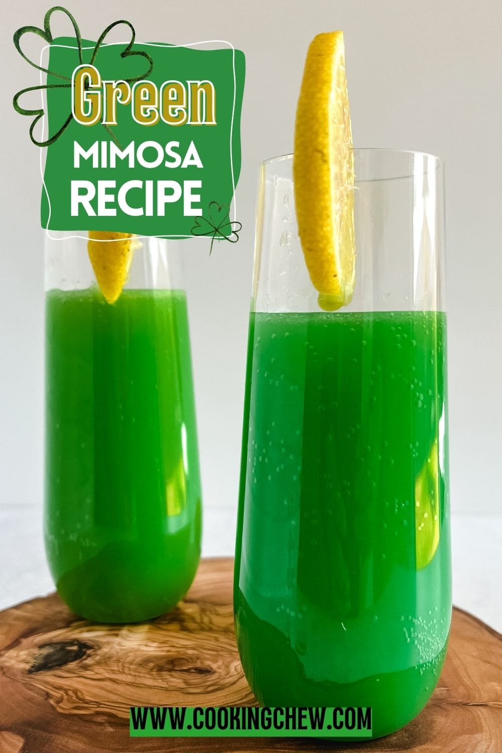 Two glasses of green mimosa with lemon slices on the rim sit on a wooden table.