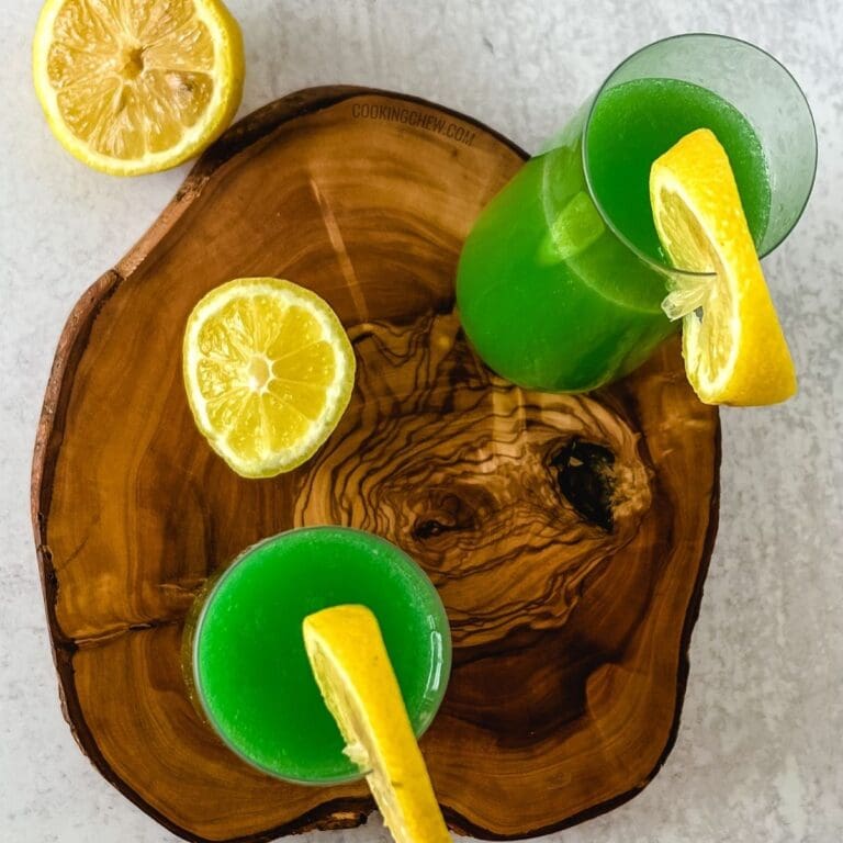 Two glasses of green colored drink with lemon slices on a wooden cutting board.