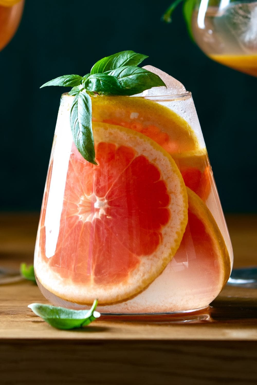 A close-up of a refreshing glass of grapefruit basil mojito with a grapefruit slice and a sprig of basil.