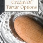 A wooden spoon rests on top of a pile of cream of tartar on a wooden table.
