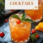 A glass of orange cocktail with a cherry and mint leaves on a slate table.