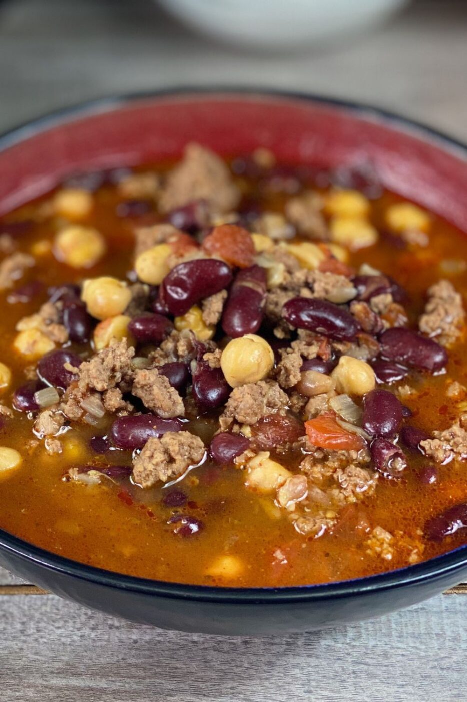 A bowl of thick, hearty three bean chili garnished with shredded cheese and a dollop of sour cream.