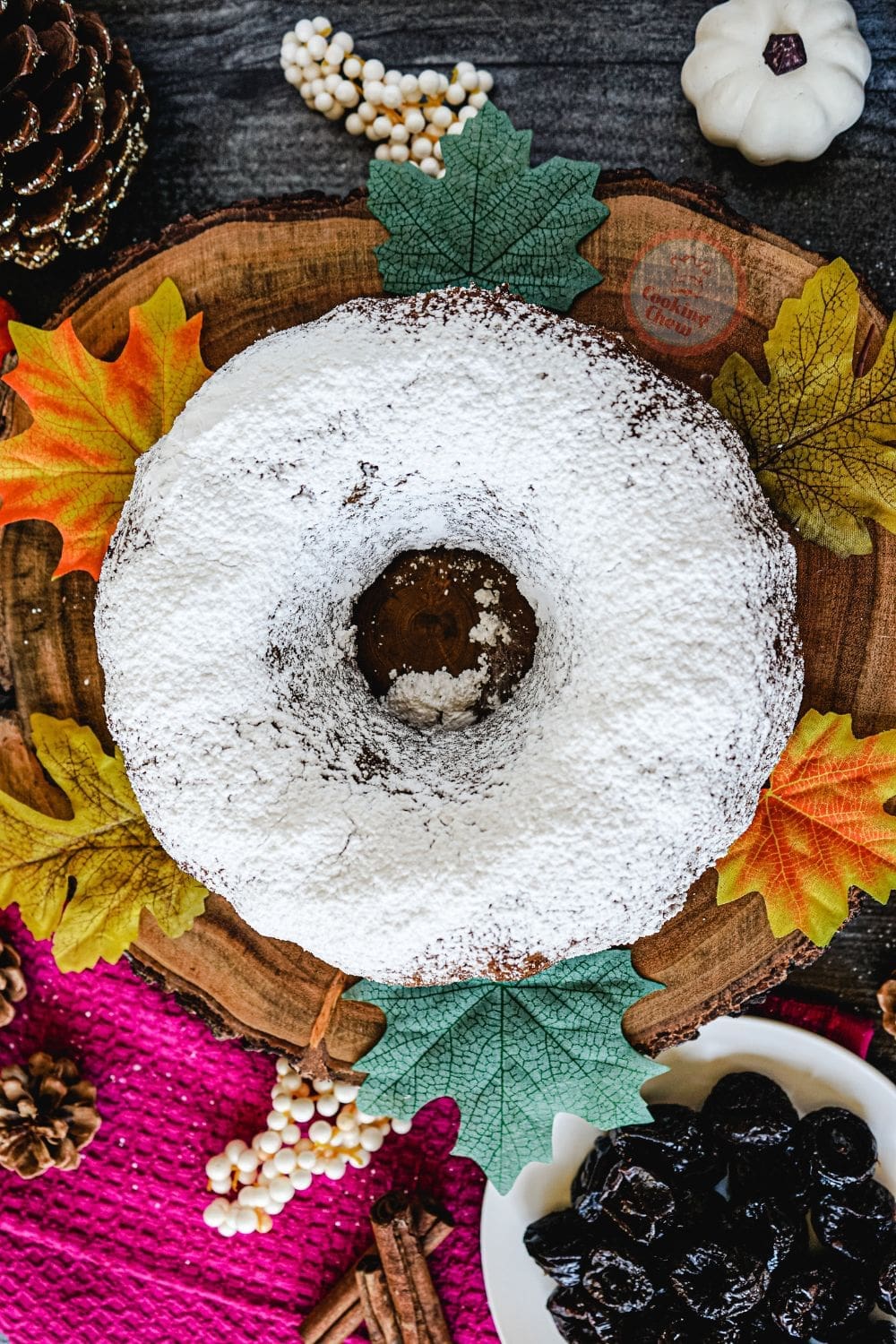 A round Christmas prune cake with a golden crust, topped with powdered sugar and a sprig of holly.