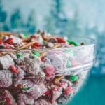 A bowl of Christmas Crunch puppy chow, a festive variation of the classic Muddy Buddies, made with Chex cereal, peanut butter, powdered sugar, and a variety of Christmas-themed sprinkles.