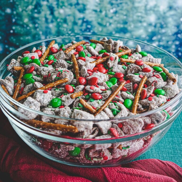 A bowl of Christmas puppy chow, also known as muddy buddies, made with chocolate Chex cereal, creamy peanut butter, and a touch of vanilla, coated in powdered sugar and sprinkled with colorful Christmas M&Ms.
